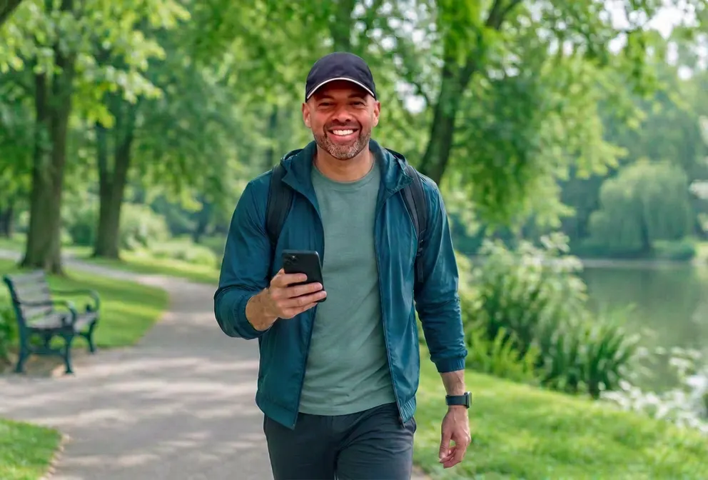 Un hombre consultando su móvil paseando por un parque